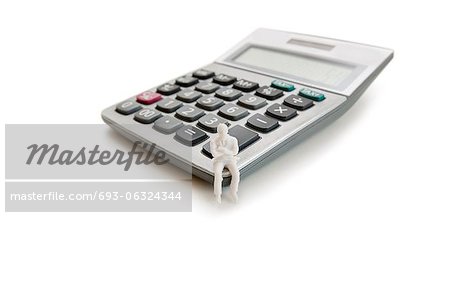 Un petit personnage mannequin assis sur une calculatrice sur fond blanc Un petit personnage mannequin assis sur une calculatrice sur fond blanc