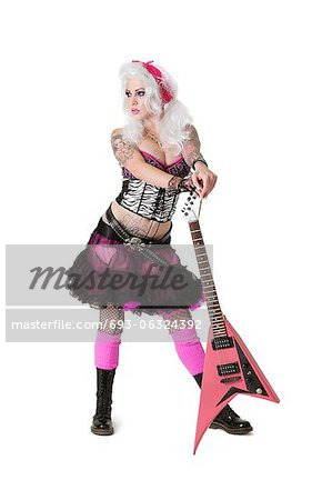 Beautiful young woman standing with guitar while looking away over white background