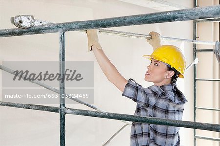 Back view of female contractor placing iron rod on scaffold
