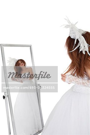 Brune en robe de mariée en regardant miroir sur fond blanc
