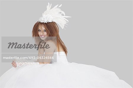 Portrait of happy young bride sitting over gray background