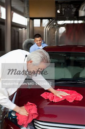 mature owner and young employee wiping vehicle with cloth in car wash