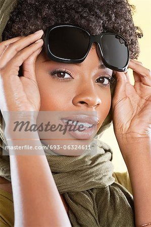 Portrait of an African American woman holding sunglasses with a stole round her neck over colored background
