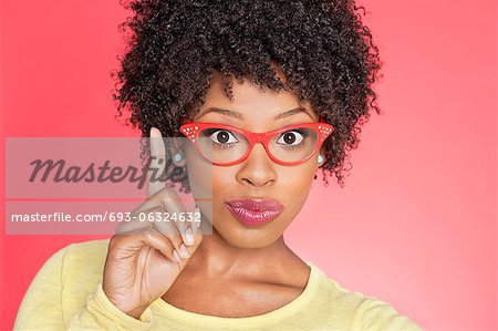 Portrait of an African American woman in retro glasses pointing upward over colored background