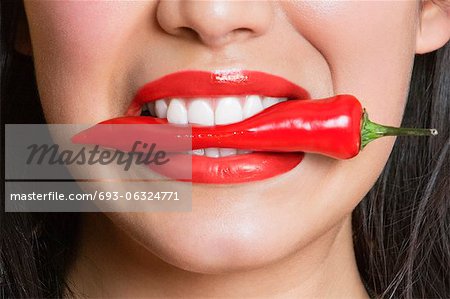 Close-up portrait of Hispanic woman biting red pepper