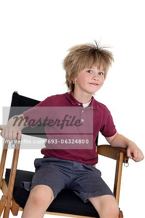 School boy assis sur la chaise du réalisateur sur fond blanc