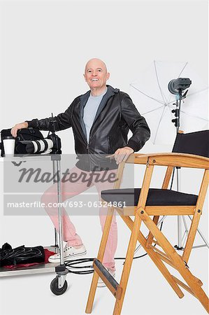 Full length portrait of a happy senior photographer with equipments in studio