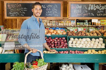 Schöner junge Mann hält Korb an Gemüse Stand im Supermarkt