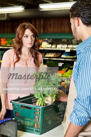 Beautiful young woman looking at store clerk in supermarket