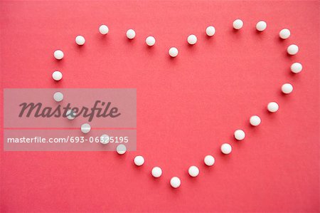 Close-up of push pins forming heart shaped over pink foreground