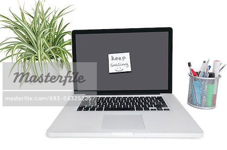 Pense-bête du visage smiley sur portable avec des fournitures de bureau et comme plante en pot Pense-bête du visage smiley sur portable avec des fournitures de bureau et comme plante en pot
