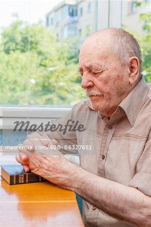 Old man praying at home near the window