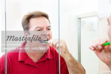 Man in his forties brushes his teeth looking in the bathroom mirror.