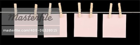 Four blank pink sticky notes held on a string with clothespins isolated on black.