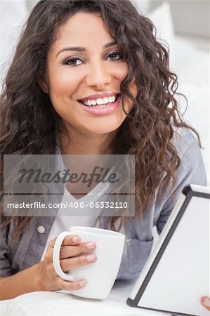 Beautiful young Latina Hispanic woman smiling, relaxing and drinking a cup of coffee or tea using tablet computer