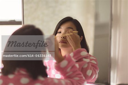 Young woman applying makeup using bathroom mirror