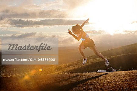 Young woman moving off starting blocks in rural setting