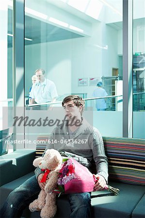 Homme dans la salle d'attente hôpital avec bouquet et ours en peluche