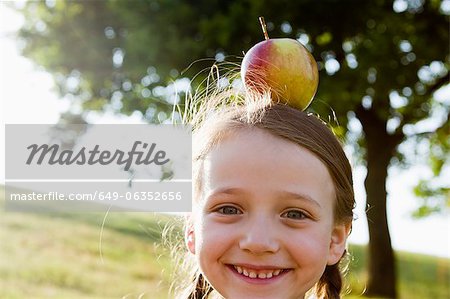 Jeune fille souriante, équilibrage de pomme sur la tête