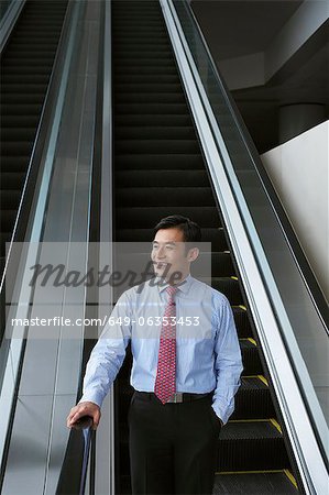 Businessman riding escalator in office