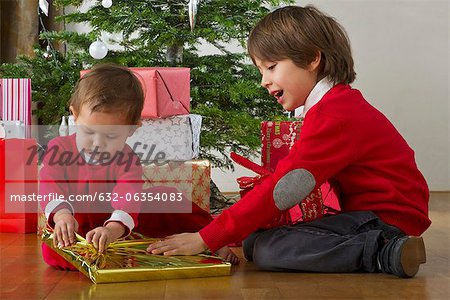Boy helping his baby sister open Christmas presents