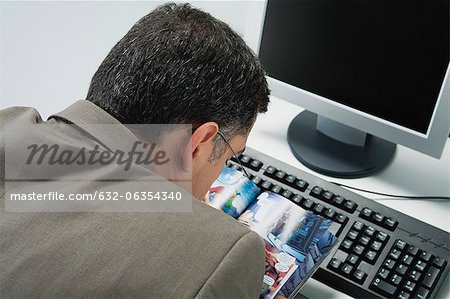 Mature man reading comic book at desk in office, rear view