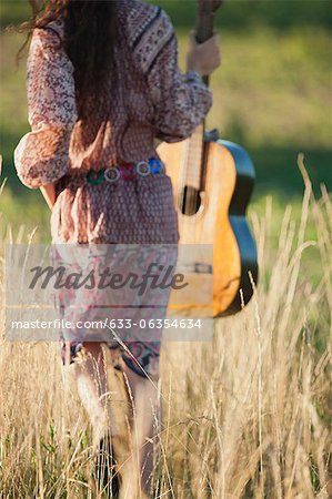 Femme qui marche à travers champ avec guitare, vue arrière