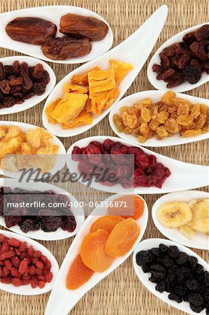 Dried fruit selection in white porcelain dishes over wicker background.