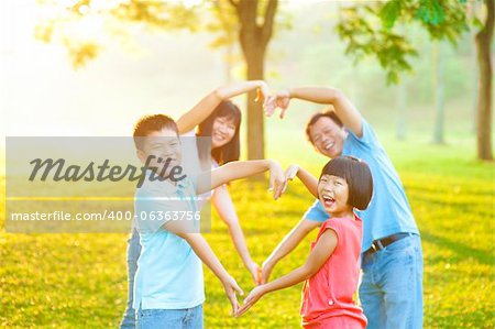 Happy playful Asian family forming love shape, outdoor green park