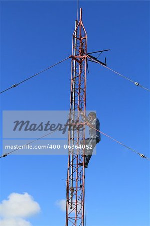 Radio tower or mast, with a worker climbing up it beneath blue sky and copy space.