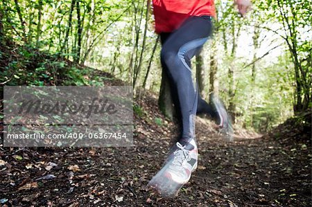 Male trail runner running in the forest on a trail. Red shirt and black pants. Summer season. Slight blur in runner to show motion. Horizontal composition.