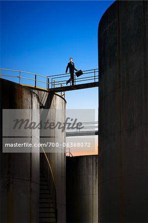 Businessman Crossing Catwalk Between Storage Tanks