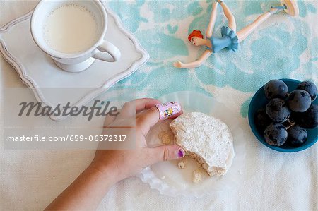 Main de la fillette, saisissant de Cookie ; Verre de lait ; Jouet Main de la fillette, saisissant de Cookie ; Verre de lait ; Jouet