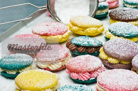 Various macaroons dusted with icing sugar on a baking tray