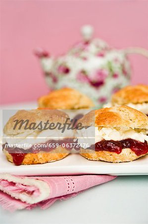 Scones with strawberry jam and cream with a pot of tea in the background