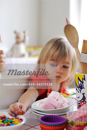 Young girl reaching for sweets from the bowl while baking