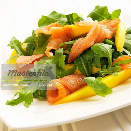 Salade de roquette au saumon et mangue sur une assiette blanche