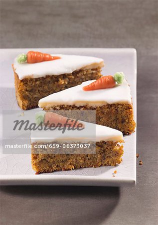 Three slices of carrot cake topped with icing and marzipan carrots