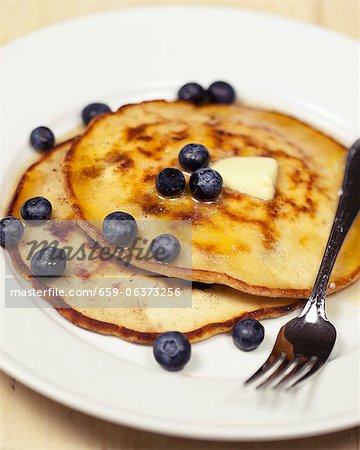 Two Coconut Blueberry Pancakes on a Plate with Melting Butter and a Fork