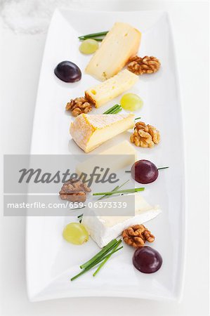 A plate of cheese specialities with walnuts, chives and grapes