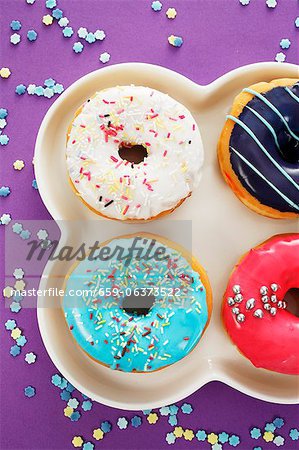 Four doughnuts with colourful glaze and sugar sprinkles