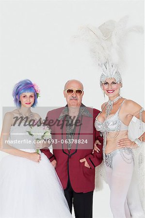 Portrait of man standing arms in arms with senior showgirl and daughter in wedding dress over gray background