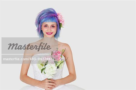 Portrait of happy young woman in wedding dress with dyed hair against gray background