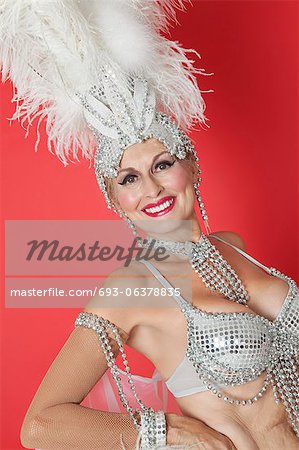 Portrait de joyeux showgirl senior avec coiffe de plumes sur fond de couleur rouge