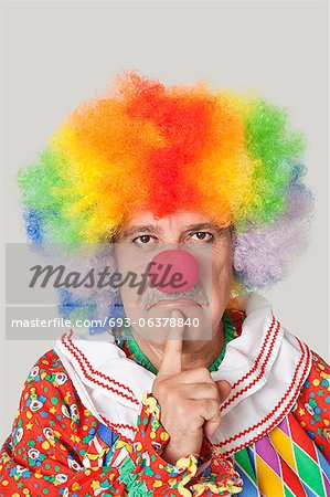 Portrait de colère clown masculin senior avec le doigt sur le menton sur fond gris clair
