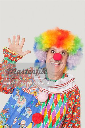 Portrait of cheerful senior male clown waving hand over gray background