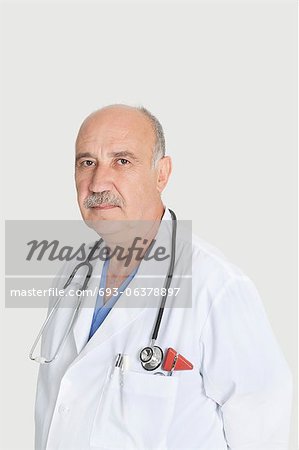 Portrait of serious senior medical practitioner over gray background