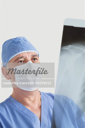 Senior male surgeon examining x-ray over gray background