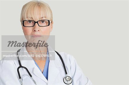 Portrait de sérieux femme médecin avec stéthoscope autour de cou sur fond gris