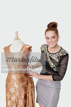 Happy young female fashion designer working on an outfit over gray background